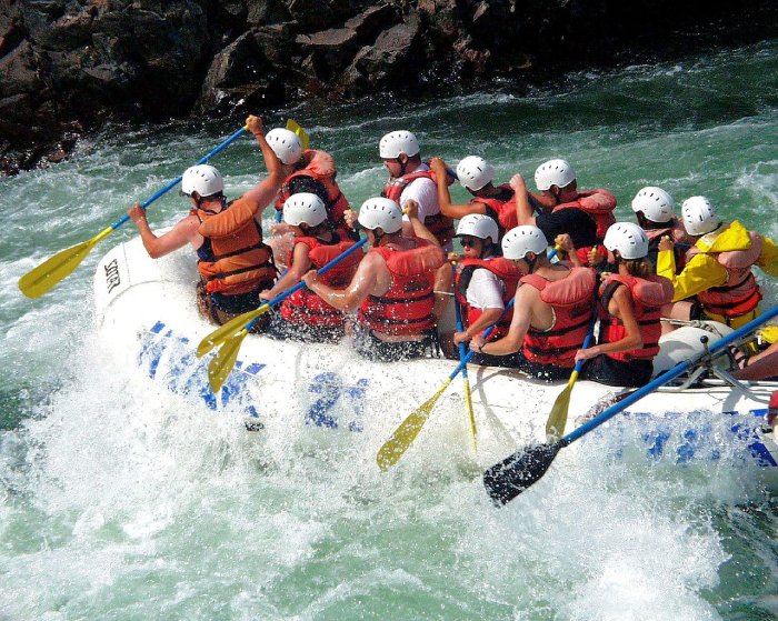 Several people wearing white rafting helmets ride the rapids during a whitewater rafting trip.