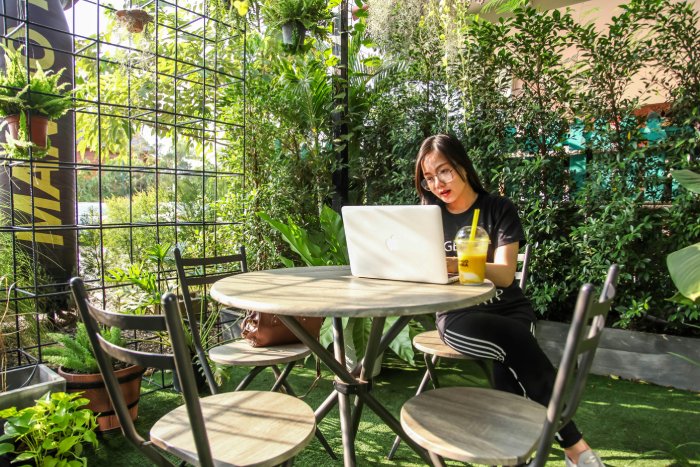 A woman works on her laptop inside a lush greenhouse.