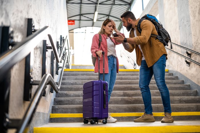 A white woman and a white man argue on a train station steps while traveling.