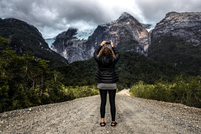 A woman takes a photo of a glacier and mountains with her smartphone.