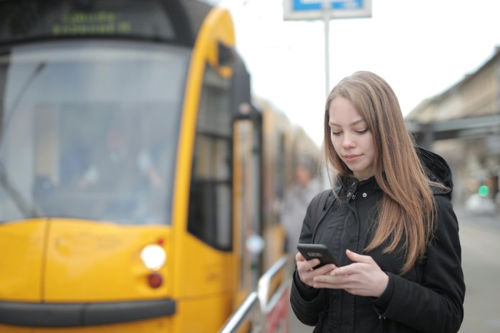 A young woman looks at her smartphone while waiting for a yellow train.