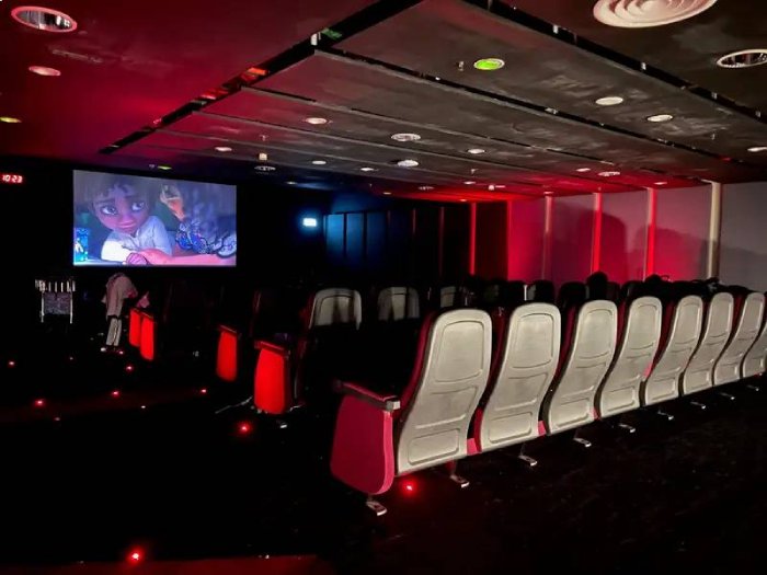 Rows of seats, dark lighting, and an animated movie playing at an airport movie theater.