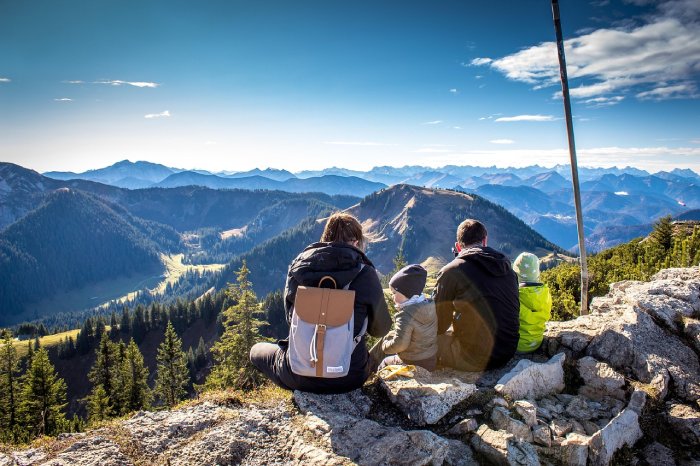 A family of four sits at the top of a mountain looking out while on a hike.