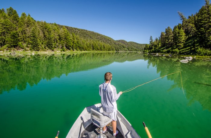 A man fly fishes from the bow of a boat in a mountain lake.