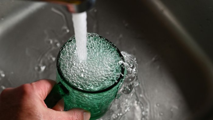 A sink faucet pours water in a green glass cup.