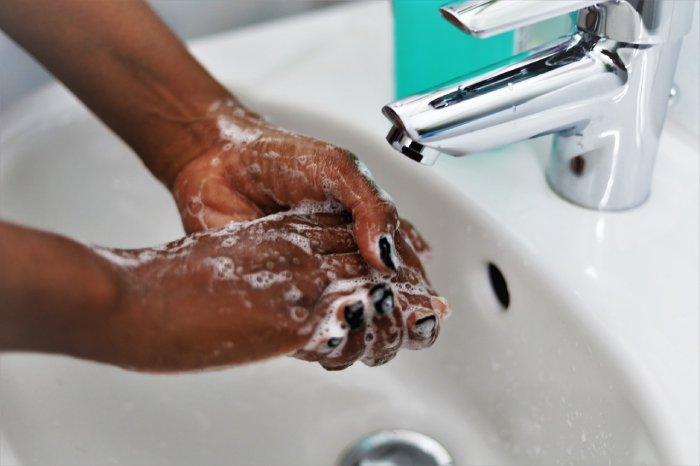 A black woman washes her hands in a sink.