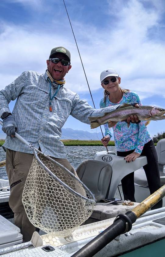 A happy man and woman catch a fish while fly fishing from a boat on a river in Montana.