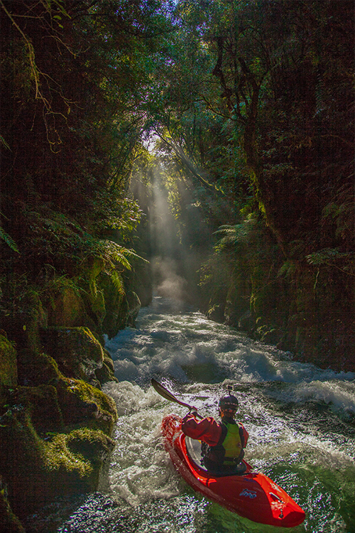person in a red kayak paddling down rapids through lush jungle