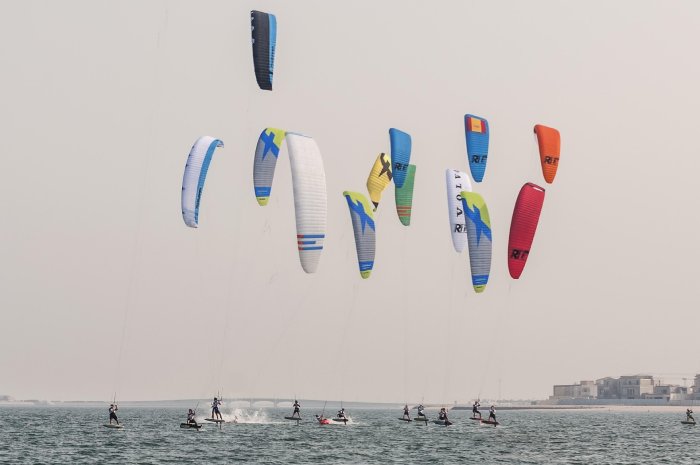 Dozens of colorful kites from kiteboarders speckle the air above kiteboarders in the ocean in Qatar.