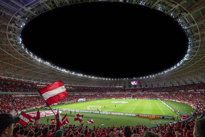 A massive soccer stadium with fans wearing red and white inside the well-lit, open-roofed round building.
