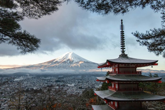 A Japanese temple high up on a hill overlooks a city with Mount Fuji in the background.