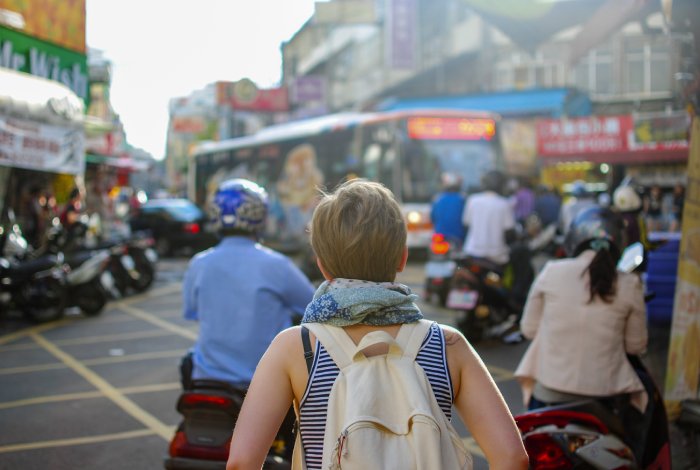 A young woman with a backpack looks out at a busy street in a foreign country.