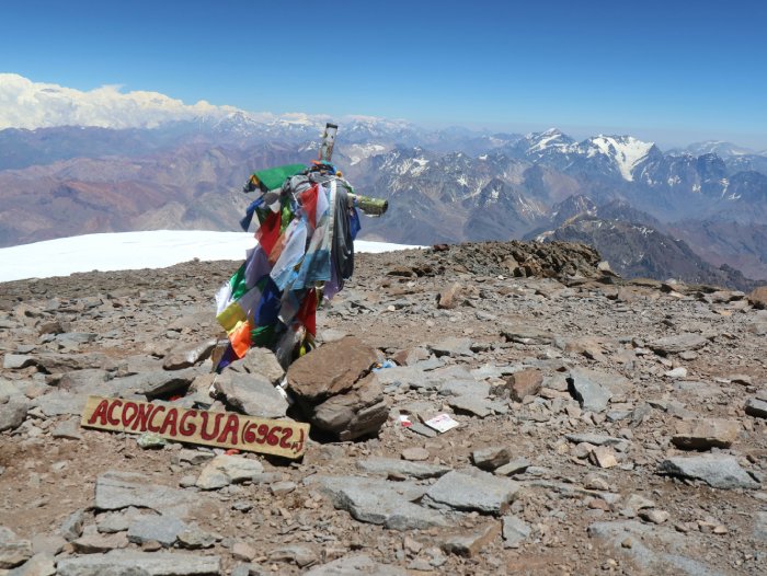 Prayer flags rest on a cross at the summit of Aconcagua on a sunny day.