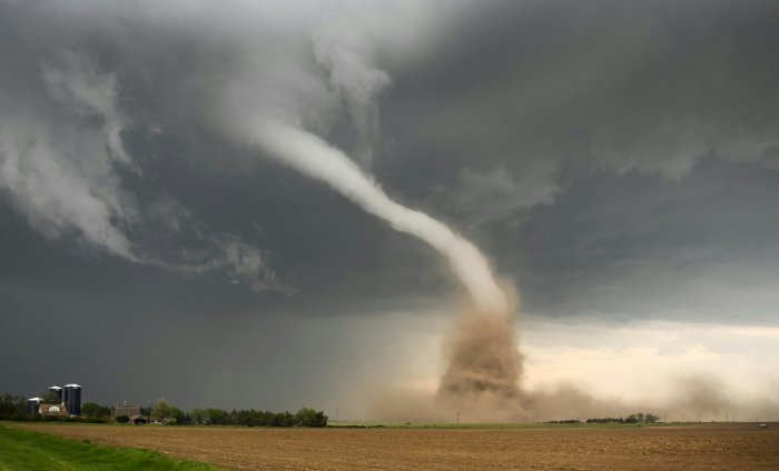A tornado sweeps across a field toward a farm.