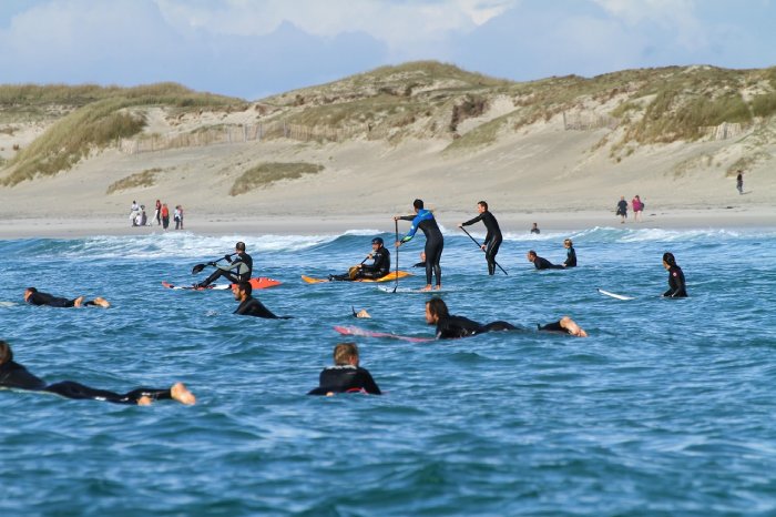 Dozens of surfers and paddleboarders wait for the next set of waves to ride while floating on their boards.